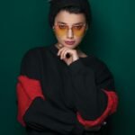 Elegant portrait of a woman in sunglasses and a knit cap with a green background.